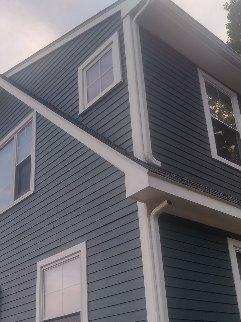 The same style of house after repair: new blue-gray lap siding, crisp white trim, soffits, gutters and downspouts